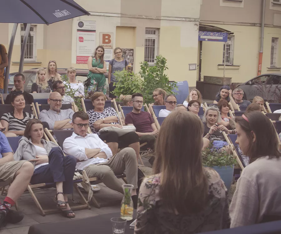Fotografia eventowa ze spotkania autorskiego z Dorotą Masłowską. Widać przybyłych siedzących do okoła autorki. 