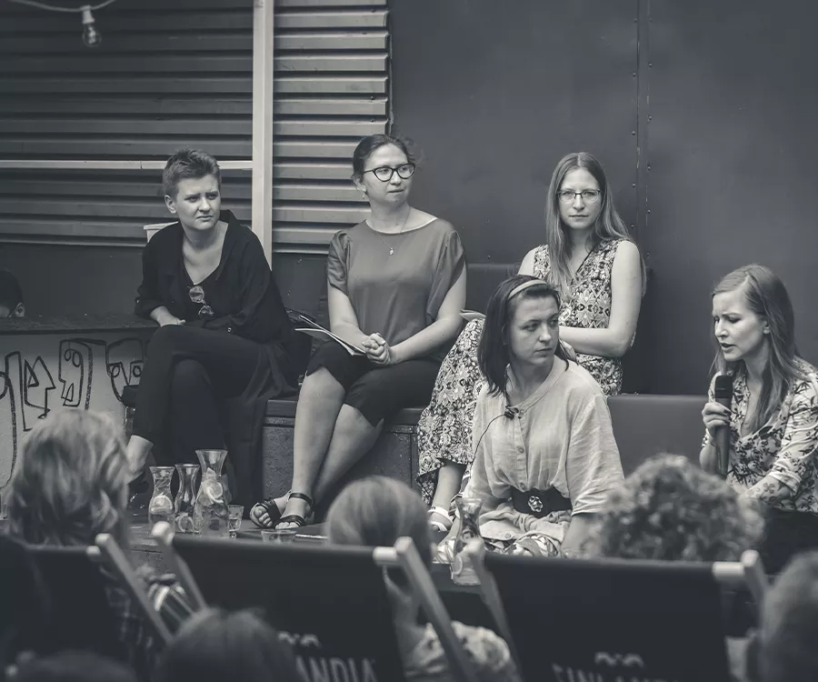 Fotografia eventowa ze spotkania autorskiego z Dorotą Masłowską. Widać autorkę oraz organizatorki spotkania.