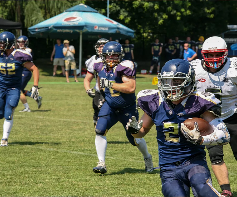 Fotografia eventowa z meczu futbolu amerykańskiego prezentująca zawodnika z piłką, w biegu