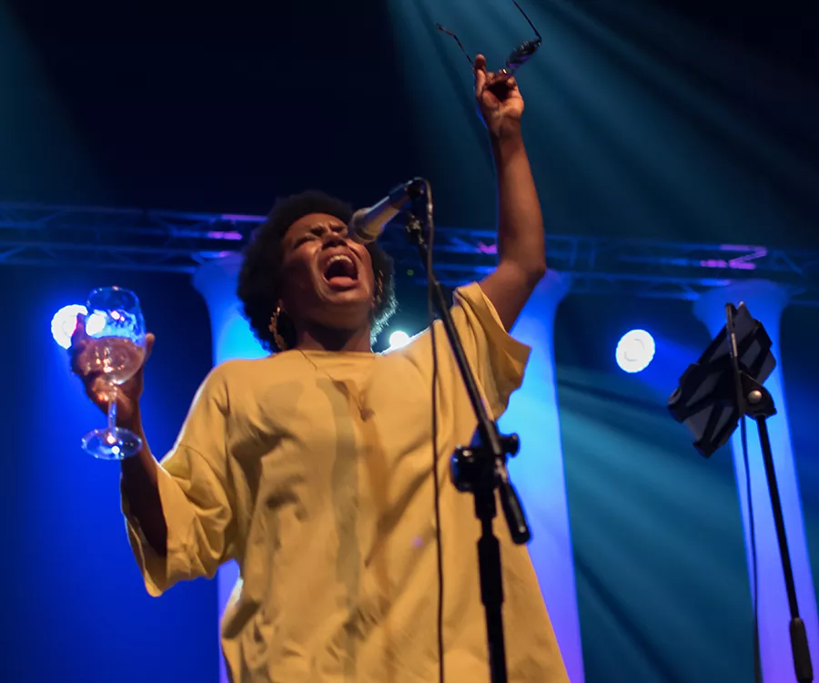 Fotografia eventowa prezentująca śpiewaczkę jazzową z kieliszkiem w jednej dłoni, okularami przeciwłonecznymi w drugiej