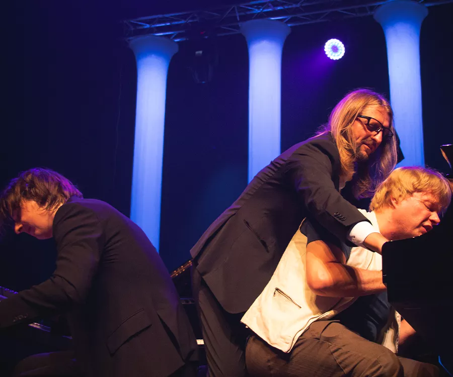 Fotografia eventowa prezentująca trio muzyków improwizujących na fortepianach 