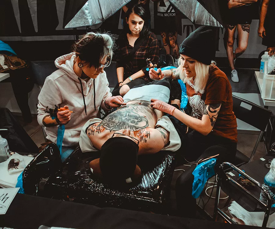 Fotografia eventowa preentująca tatuowanie pleców przez dwie tatuatorki jednocześnie 