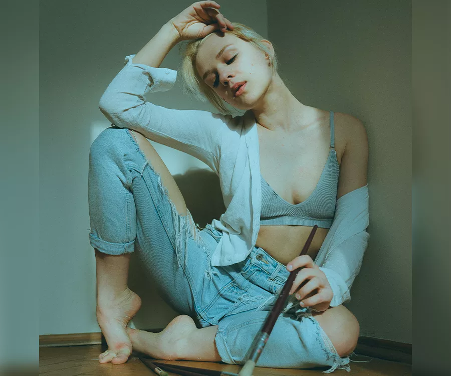 Portret dziewczyny siedzącej w rogu pokoju, trzyma duży malarski pędzel