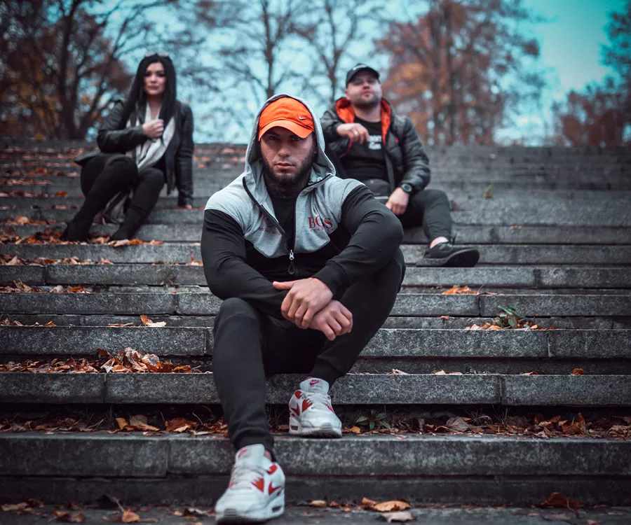 Trzy osoby siedzące na schodach w jesiennej scenerii, otoczone kolorowymi liśćmi i przyjemnym światłem.