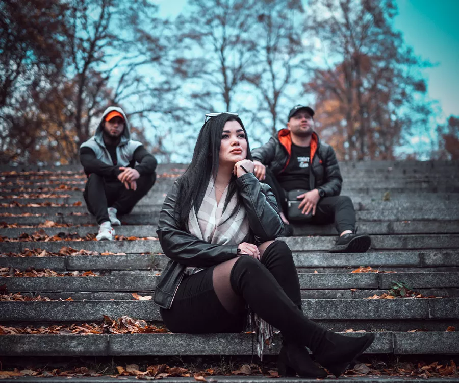 Trzy osoby siedzące na schodach w jesiennej scenerii, otoczone kolorowymi liśćmi i przyjemnym światłem.