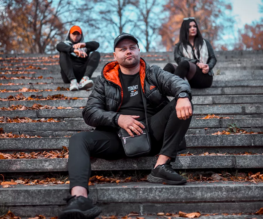  Trzy osoby siedzące na schodach w jesiennej scenerii, otoczone kolorowymi liśćmi i przyjemnym światłem.