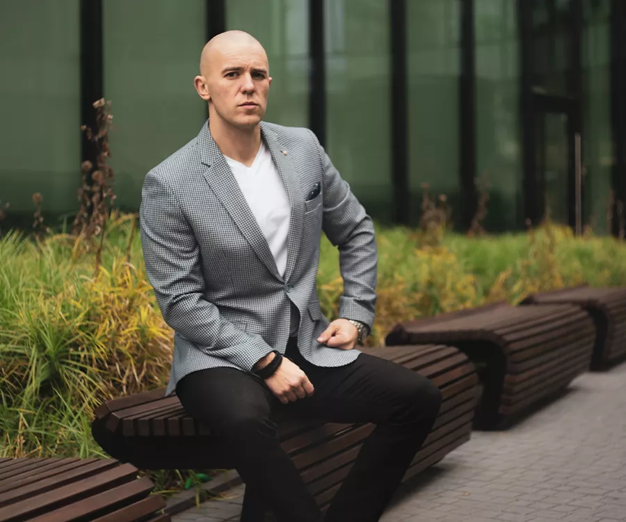 Portret eleganckiego mężczyzny siedzącego na ławce, w tle biurowiec.