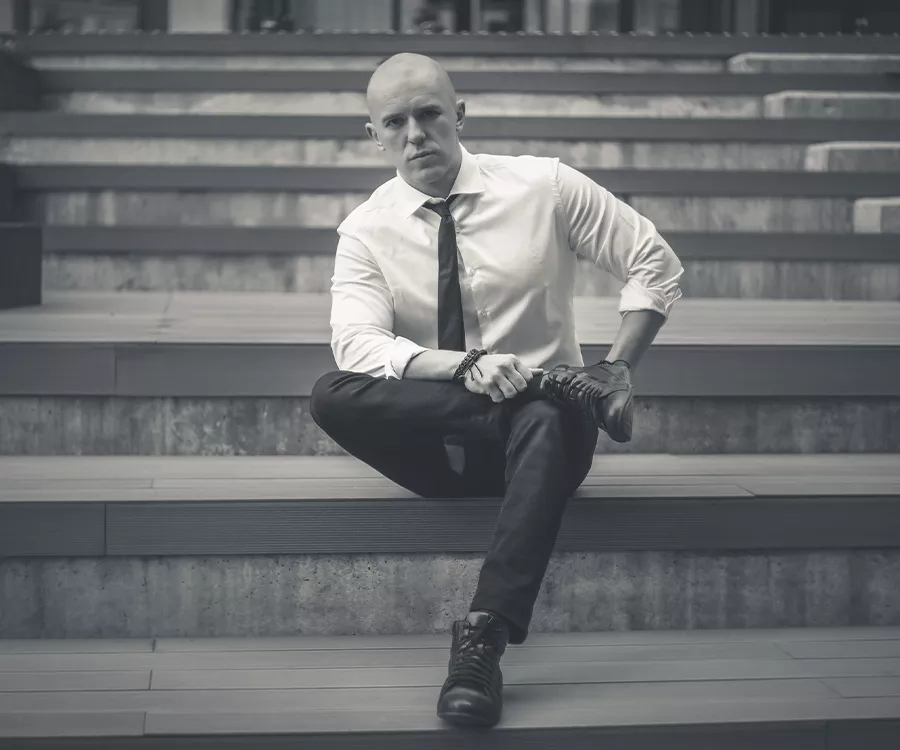 Portret meżczyzny, w białej koszuli, siedzącego na schodach.