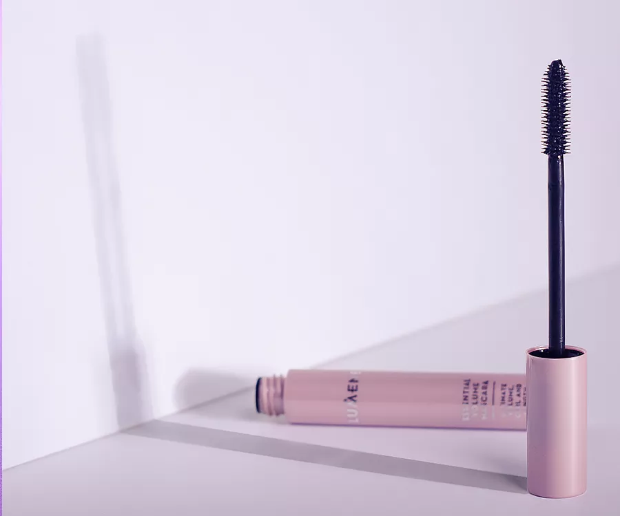 Zdjęcie produktowe przedstawiające mascare i szczoteczkę. Szczoteczka jest postawiona pionowo, opakowanie leży
