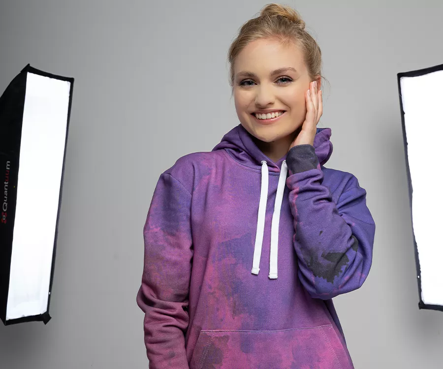 Zdjęcie produktowe przedstawiające uśmiechnięta dziewczynę w studiu fotograficznym, ubraną w bluzę allover print, w odcieniach fioletu