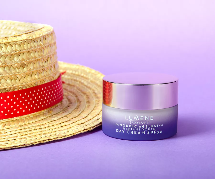 Zdjęcie produktowe przedstawiające kapelusz słomkowy, a obok niego fioletowy słoiczek kremu, zrobiony z mrożonego szkła.