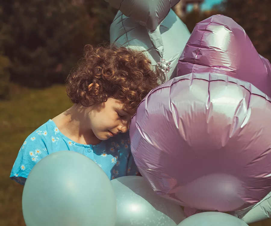 Zdjęcie dziewczynki wtulonej w balony. Widać zadumę. 