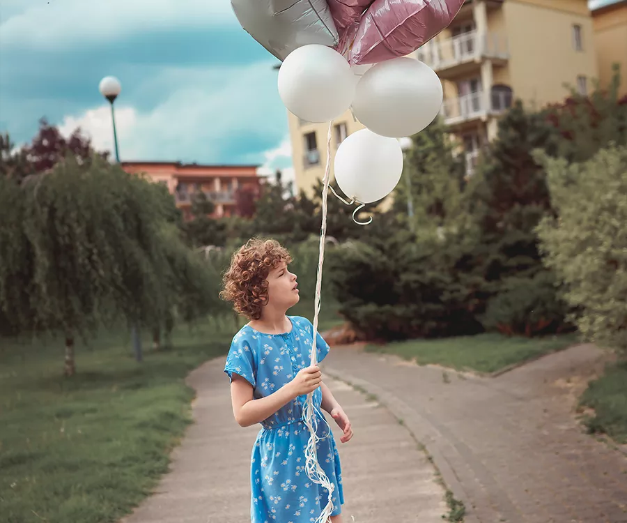 Fotografia rodzinna przedstawiająca dziewczynkę w sukience w kwiatki, trzymającą unoszące się balony. 