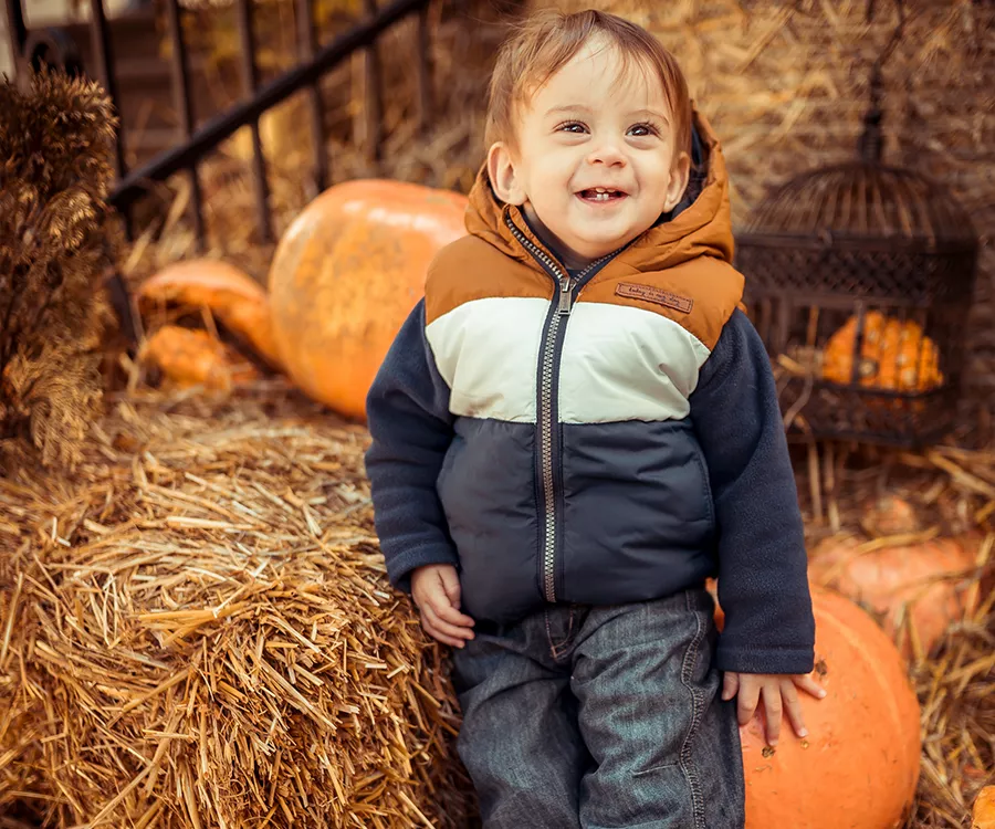 Fotografia rodzinna przedstawiająca uśmiechniętego chłopca w otoczeniu siana i dyń 