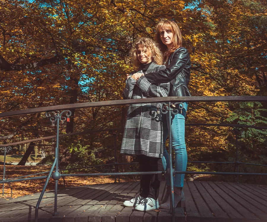 Fotografia rodzinna przedstawiająca mamę z córką stojące na mostku, w tle jesienny park