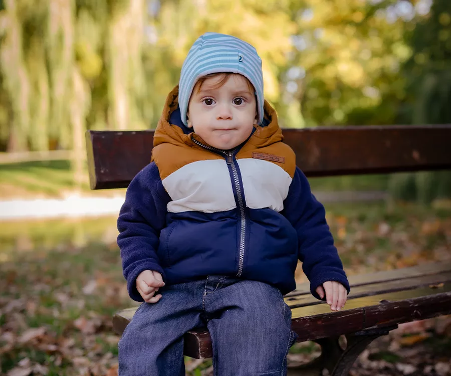 Fotografia przedstawia małego chłopca siedzącego na ławce, w tle jesienny park 