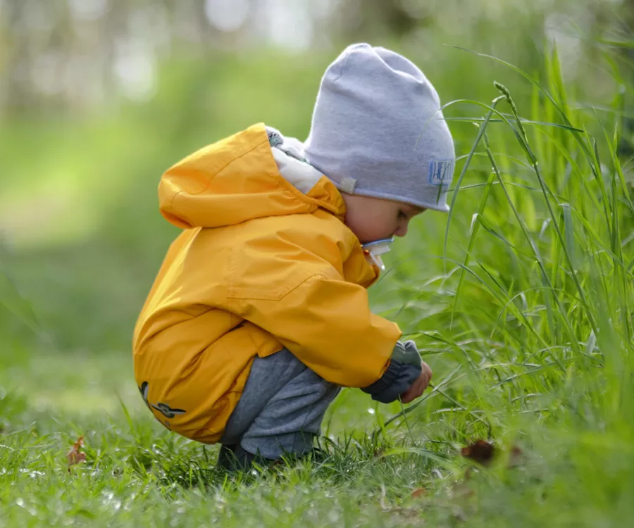Fotografia rodzinna przedstawiająca chłopca pośród lasu, kucającego i zaintrygowanego czymś w trawie. 