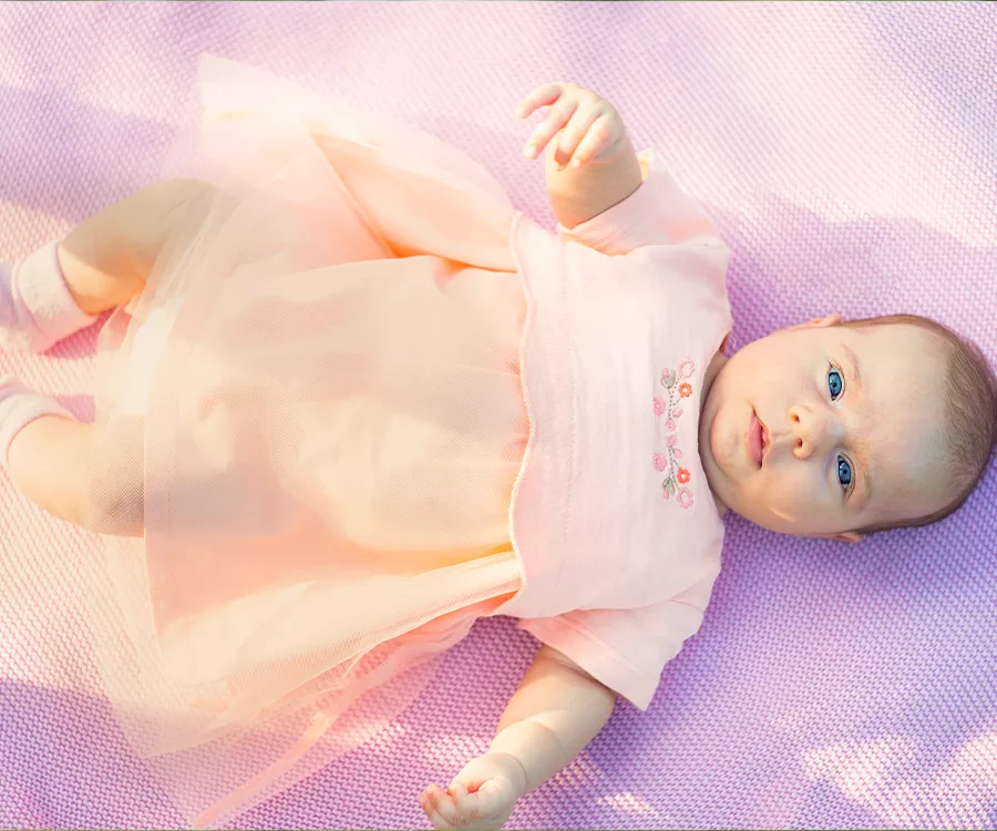 Fotografia rodzinna przedstawiająca leżącą na plecach, kilku miesięczną dziewczynkę, leży na fioletowym kocyku i ma na sobie sukienke. 