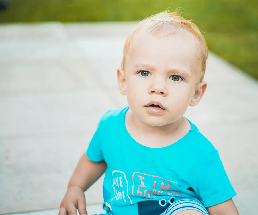 Zdjęcie przedstawiające około dwuletniego chłopca w jasnej błekitnej koszulce, chłopiec patrzy prosto w obiektyw 