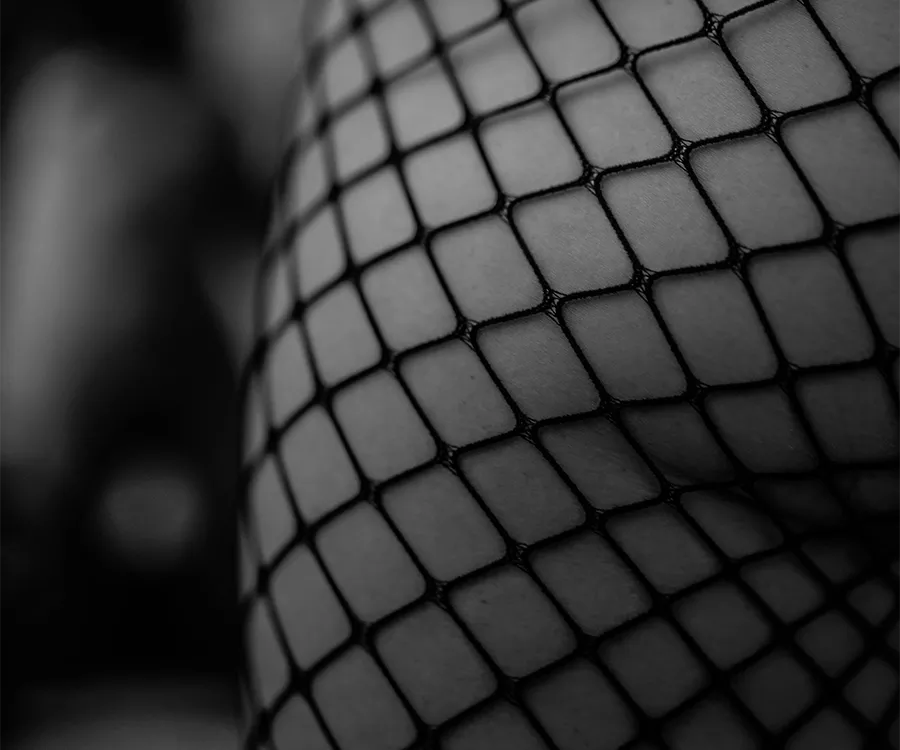 Na pierwszym planie fragment pośladka w kabaretkach, w tle widać rozmytą postać kobiety odbitą w lustrze