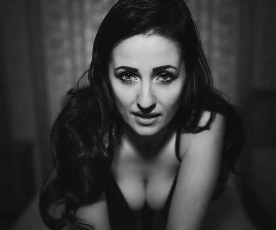 Fotografia przedstawiająca kobietę o dużych oczach patrzącą wprost w obiektyw z bardzo bliska. Klęczy na łóżku