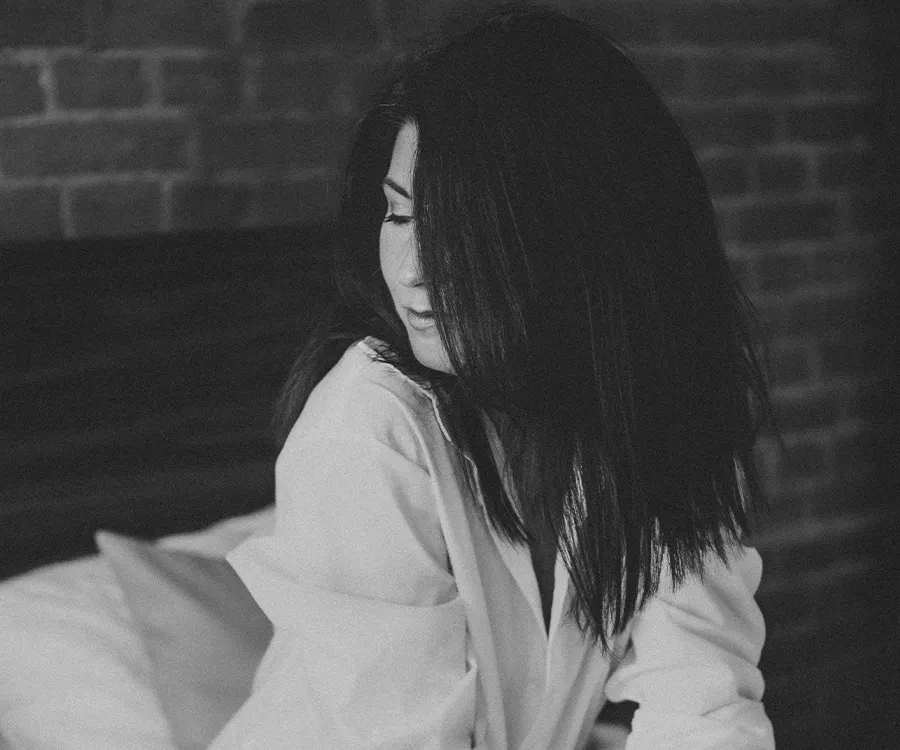 Fotografia sensualna kobiety ubranej jedynie w białą męską koszulę. Siedzi na dużym łóżku