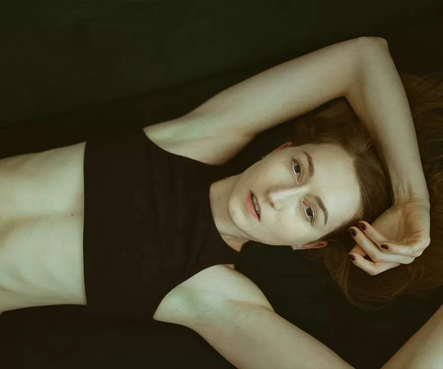 Fotografia dziewczyny w czarnym topie, leżącej na kanapie, zdjęcie wykonane od góry