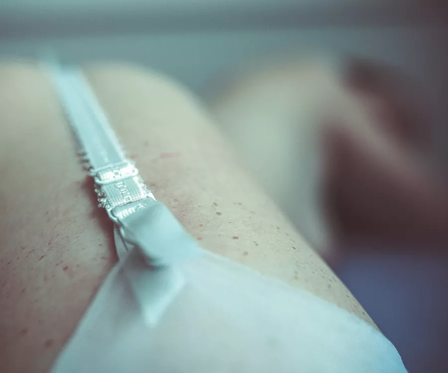 Na pierwszym planie białe zapięcie do pończoch, w tle leżąca półnaga dziewczyna