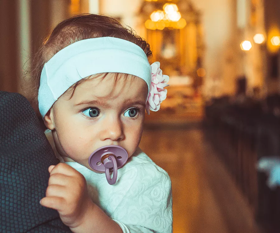 Zdjęcie małej dziewczynki na rękach ojca, na tle wnętrza kościoła, przed chrztem