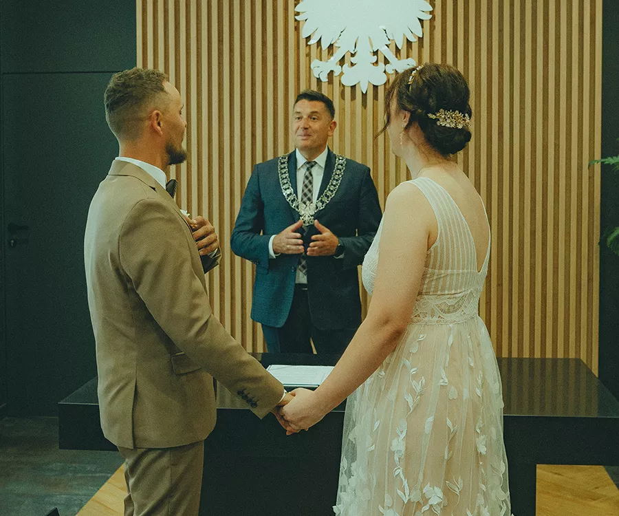 Para młoda trzymająca się za dłonie, stoją przed urzędnikiem USC